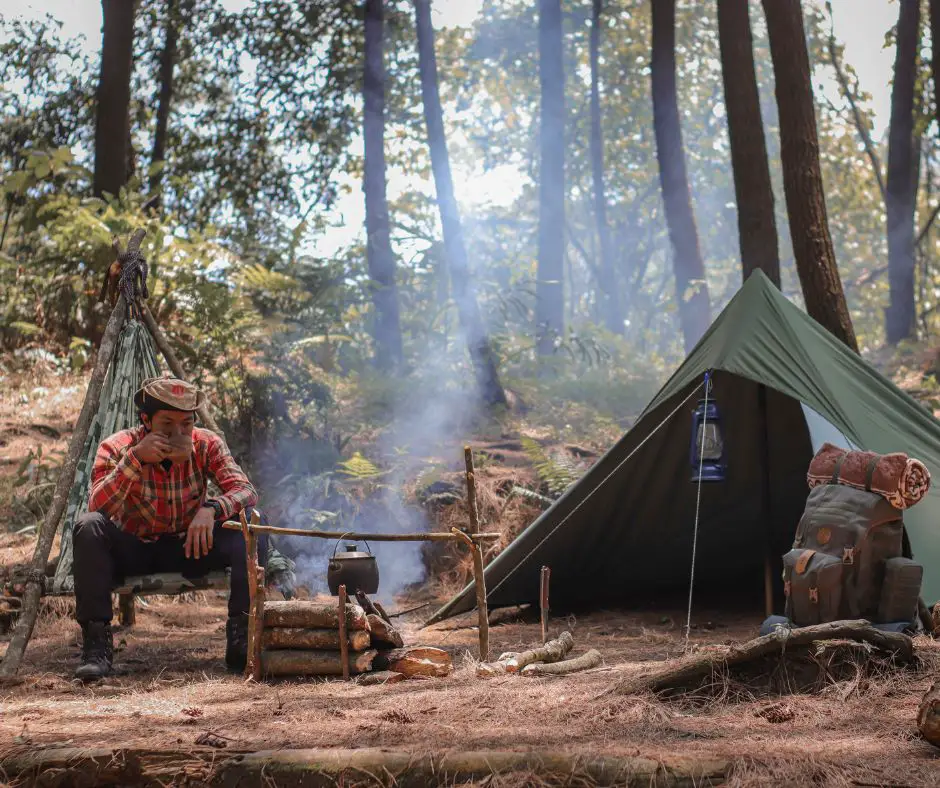 A man is sitting near fire and tent