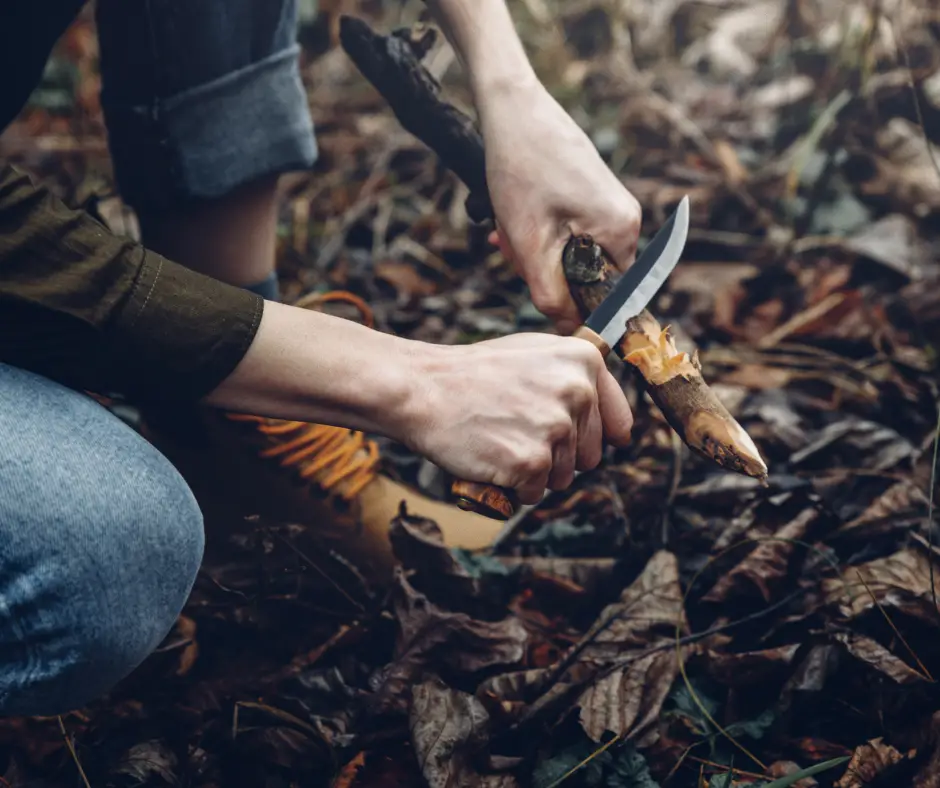 A woman using bushcraft knife to carve wood for fire